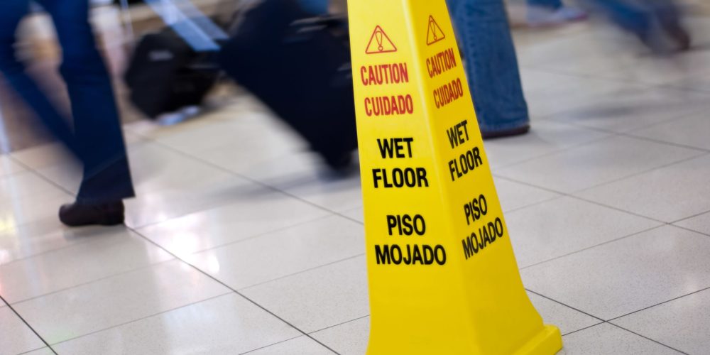Picture of a Caution Wet Floor yellow cone sign with blurred motion people walking in the background