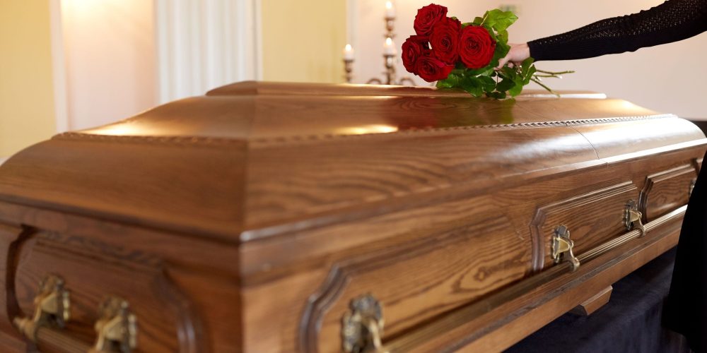 people and mourning concept - woman with red roses and coffin at funeral in church